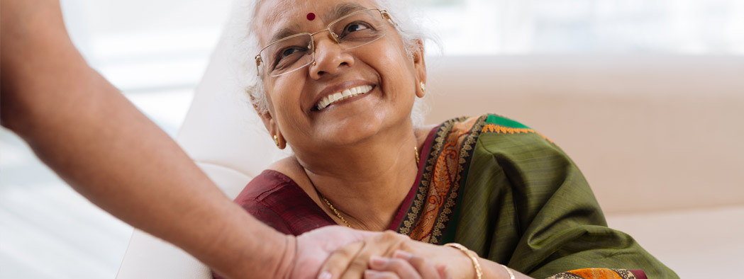 Female senior looking up smiling shaking an individual’s hand indoors