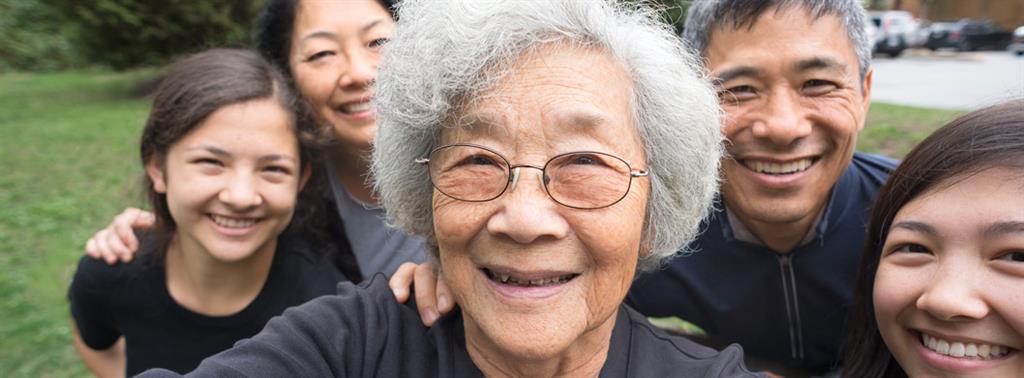 Female senior outside taking a selfie with son, daughter and grandchildren behind her