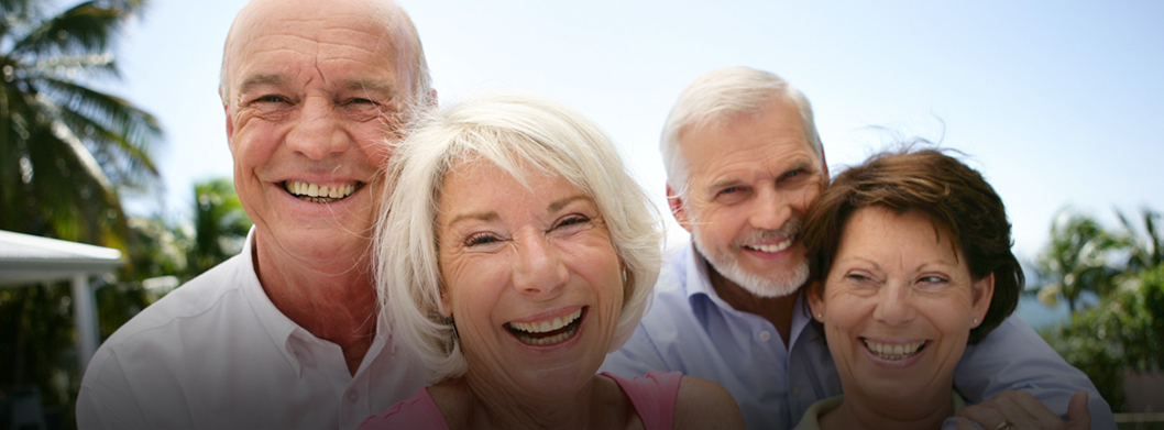 Two older adult couples , looking happy with a palm tree in the background